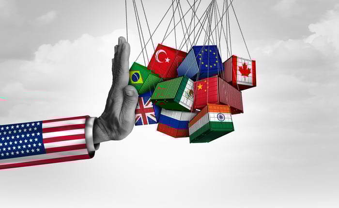 A hand dressed in an American-flag sleeve blocks several trade containers featuring various international flags.