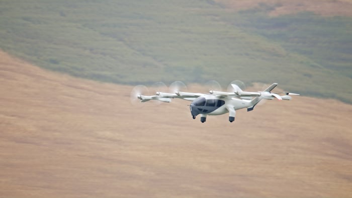 An Archer Aviation eVTOL flying over a hilly landscape.
