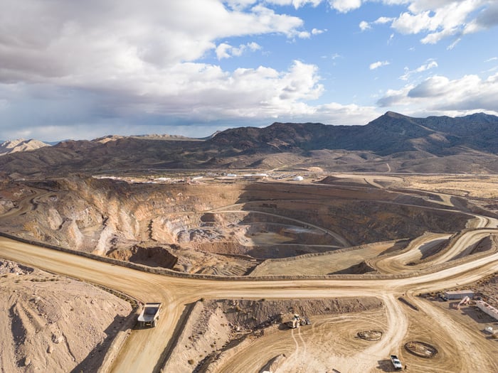 Wide angle shot of an open pit mine, with terraced shelves and a truck on a road. 