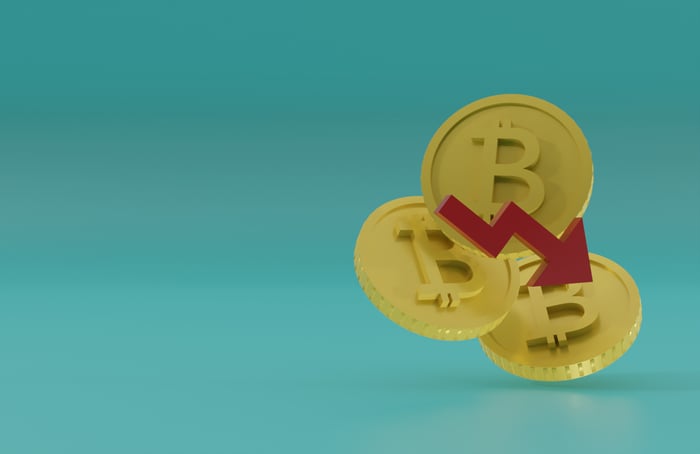 Three Bitcoins with a downward arrow on a blue background. 