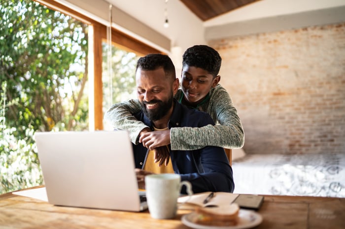 Young boy hugging his father as the two check out something on a laptop at home. 