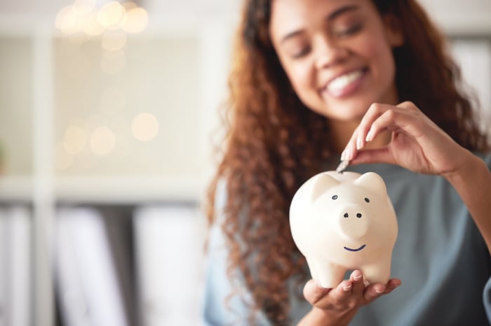 Person stuffing money into a piggy bank and smiling.
