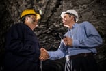 Two people smiling and shaking hands while inside a mine