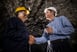 Two people smiling and shaking hands while inside a mine