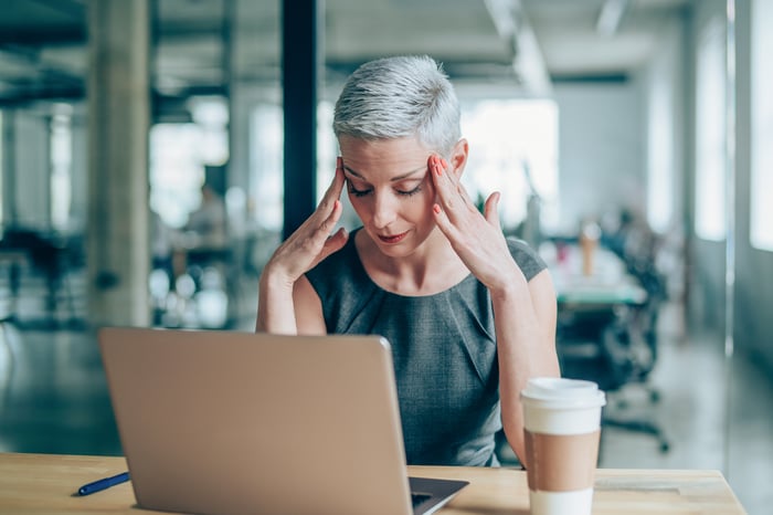 A concerned person places their fingertips on their temples while looking at a laptop.