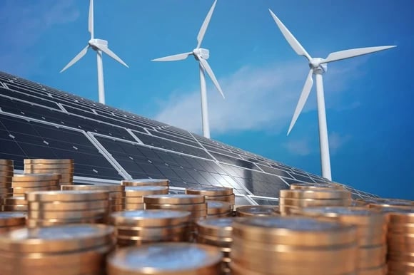 Wind turbines spin over a roof covered in solar panels, with piles of coins in front.