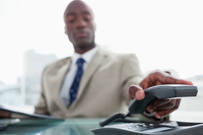 A person in an office lifts the handset of a desk phone.