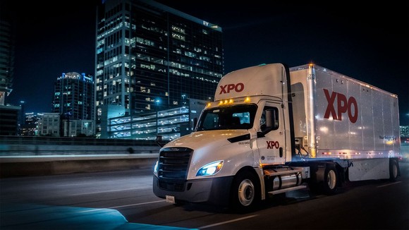 An XPO truck driving through a city at night.