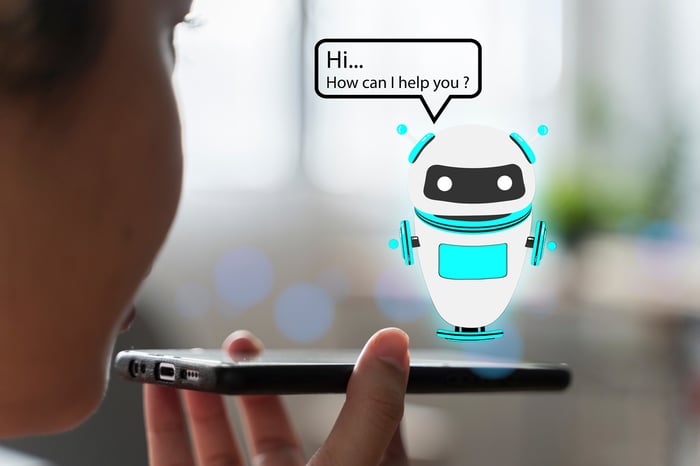 A person speaks to their smartphone, with a holographic robot hovering above the screen.
