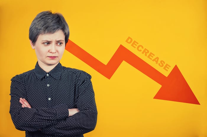 A person stands with their arms folded, looking at a descending arrow.