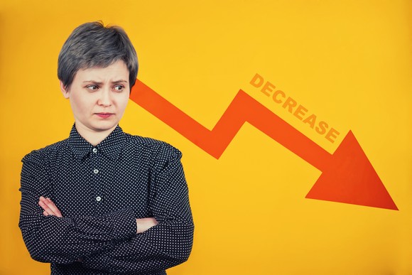 A person stands with their arms folded, looking at a descending arrow.