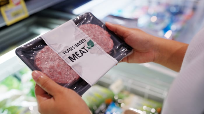 A shopper inspects a package of plant-based meat in a grocery store.
