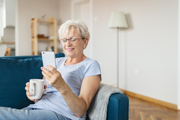 Smiling person holding coffee mug and looking at smartphone.