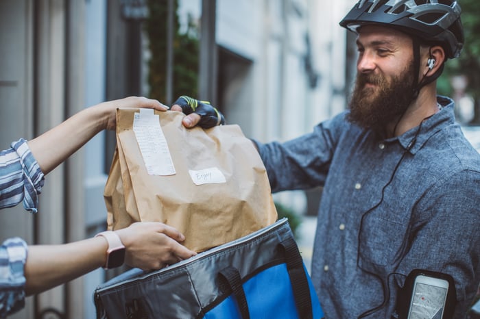 A food delivery person hands a food order to another person. 