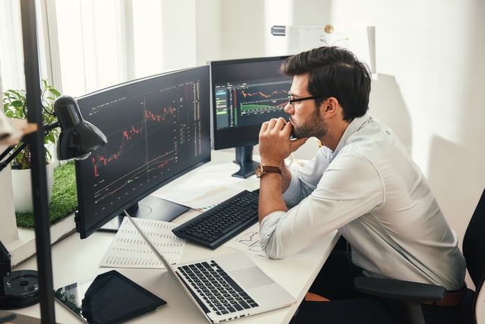 Person sitting at a desk looking at two monitors displaying stock charts.