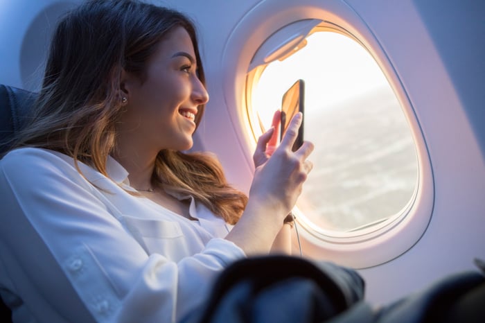 A person holding a smartphone is looking out of an airplane window.