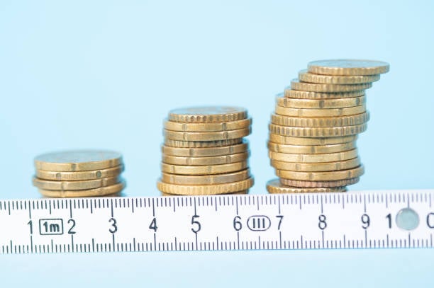 Three piles of coins, each one bigger than the last, arranged against a role of measuring tape.