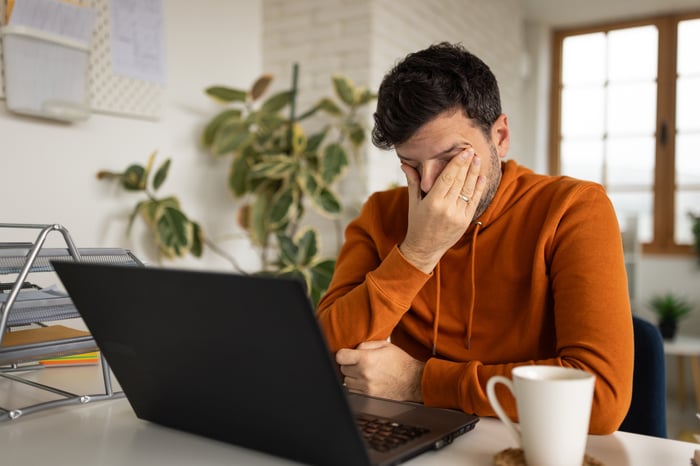 Man looking at laptop with hand on his face. 