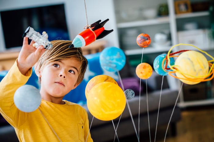 A child plays with a toy rocket and solar system model.