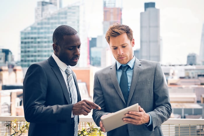 Two people in business dress looking at a tablet.