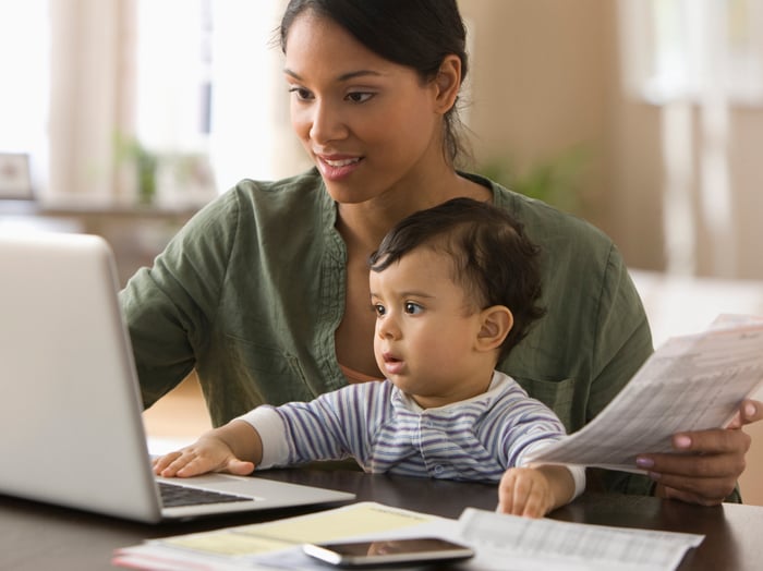 A person sitting with their child, looking at a laptop.