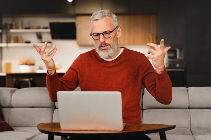 A person looking at a laptop, raising their arms as if frustrated.