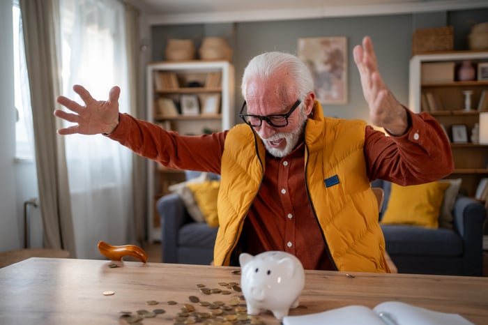 A person looks at a piggy bank and a pile of coins on a desk.