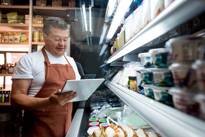 A person in an apron standing by a food aisle.