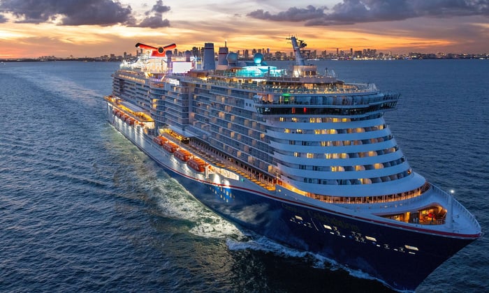 carnival cruise line ship at sunset with lights on.