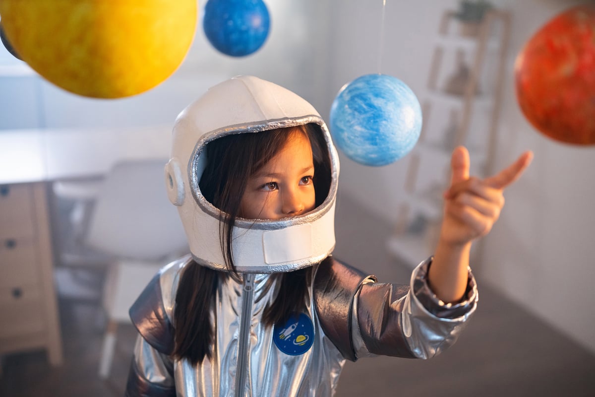 girl dressed as astronaut plays with solar system model.