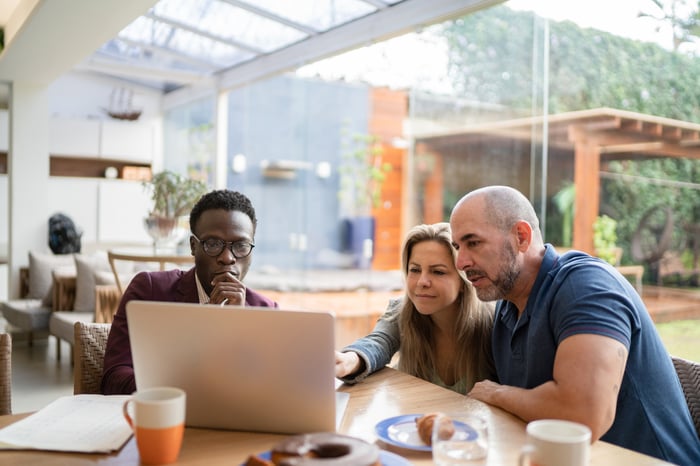 Three investors sitting in a cafe gather around a laptop and discuss some figures.