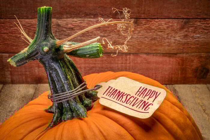A pumpkin sits on a wooden surface, with a Happy Thanksgiving tag tied to its stem.