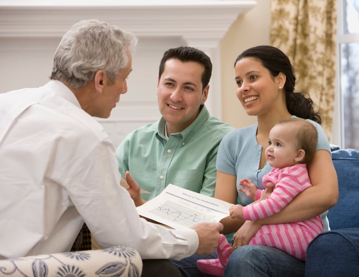 Three people discussing paperwork, with one holding a baby.
