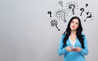 question marks over woman's head while holding smartphone.