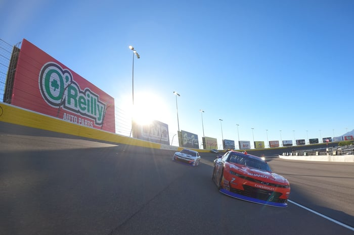 Racecars drive past an O'Reilly Auto Parts sign on the wall of a NASCAR track.