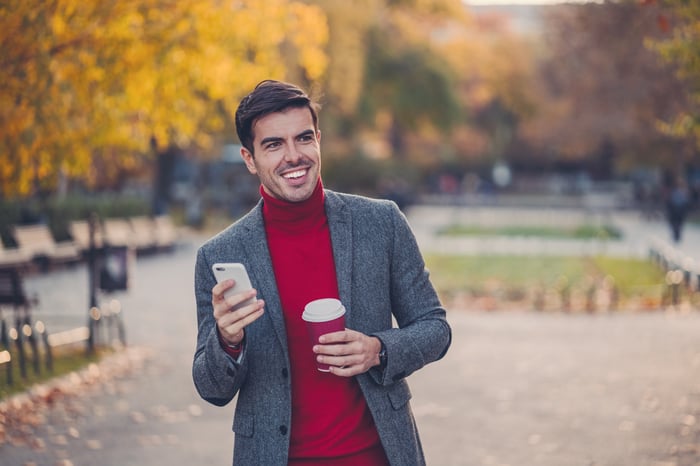 An investor, holding a phone, walks in a park during the fall. 