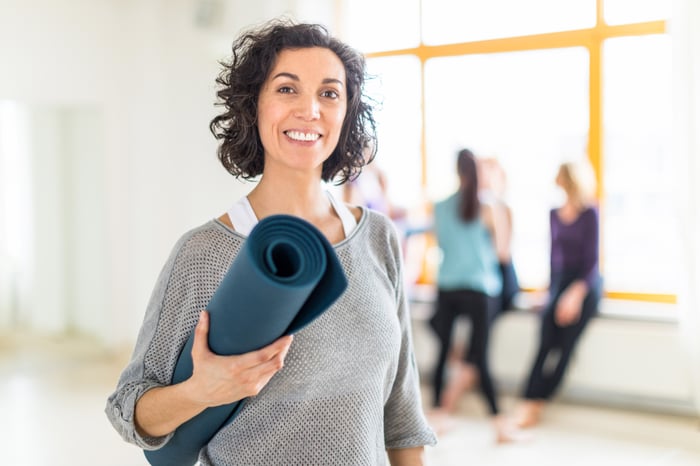 Person in yoga studio, holding rolled-up mat.