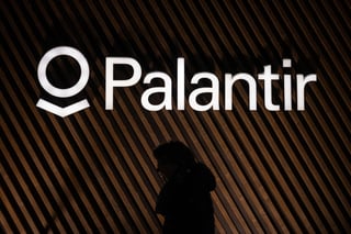 Person walking past a Palantir logo on a wall.