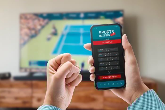 Person watching tennis and holding a phone with a sports betting app open.