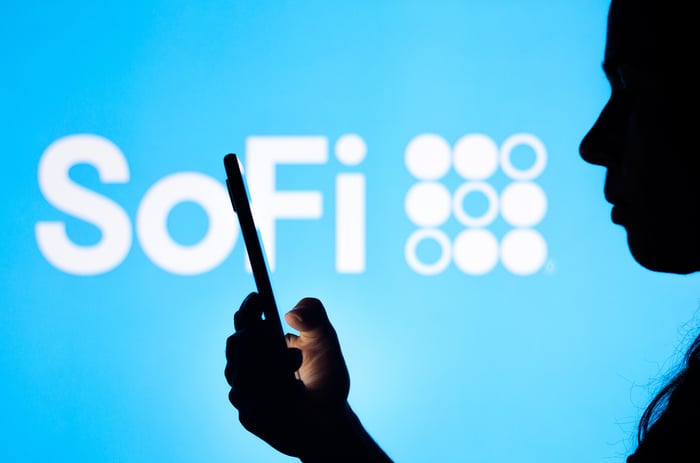 A person holding a smartphone with the SoFi logo in the background.
