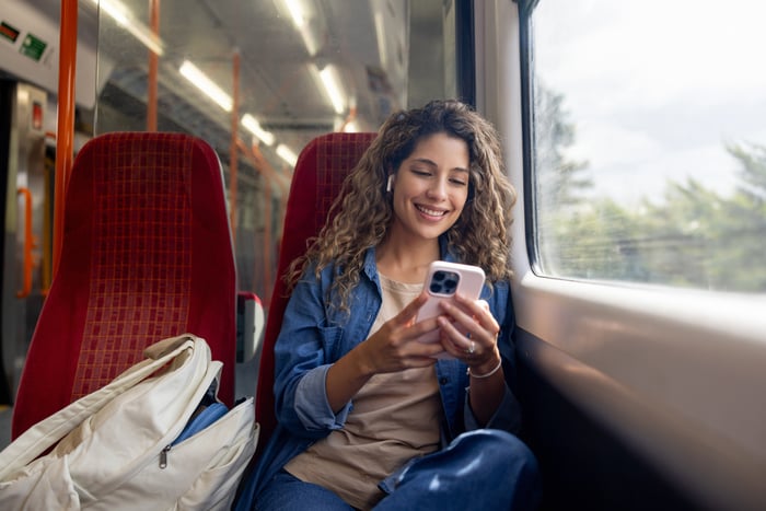 A person smiles while looking at their cell phone on a train.