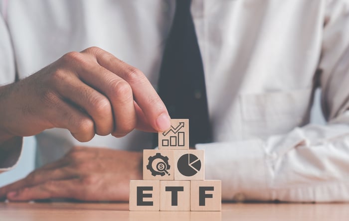 Someone stacking wooden blocks labeled ETF with icons of growth, money, and a pie chart.