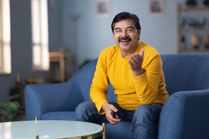 Man wearing a sweater and sitting on a blue couch.