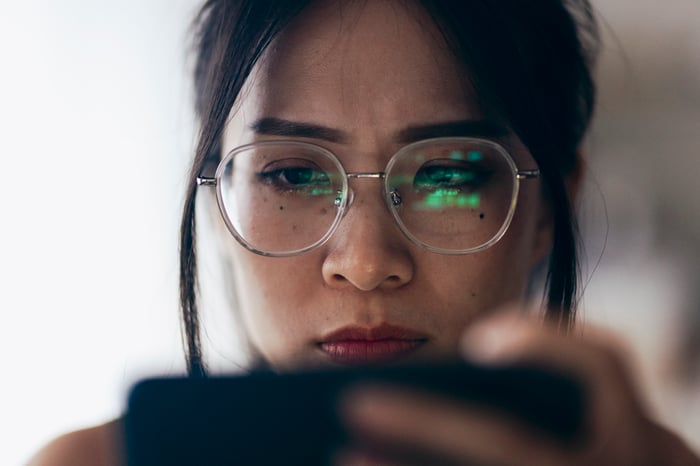 A person looking at their phone, with the reflection of a stock chart in their glasses