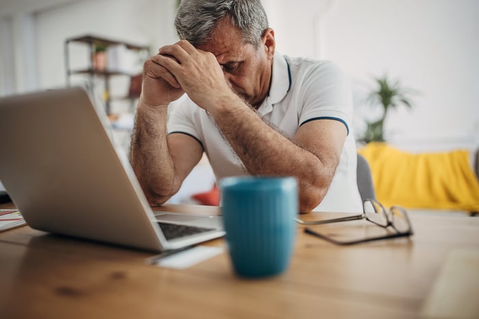 Stressed person with head on hands sitting in front of laptop.