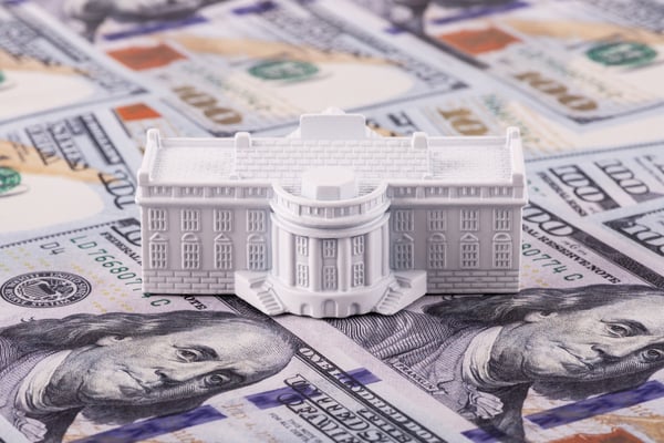 A toy White House on top of one-hundred-dollar bills. 