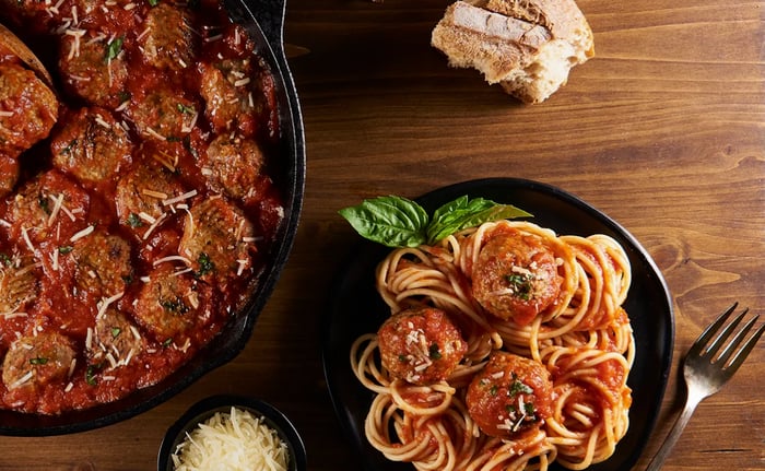 Spaghetti, meatballs, bread, and cheese are on a wooden table. 