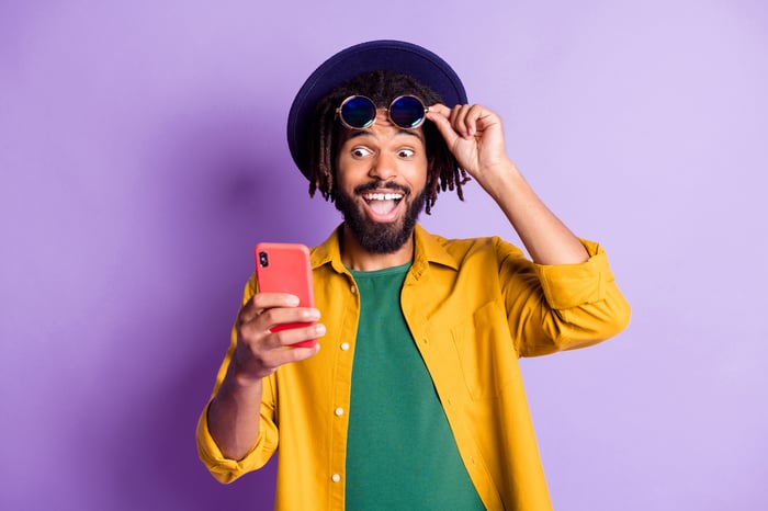 Happy investor in colorful outfit looking at smartphone.
