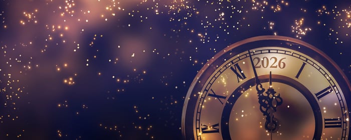 Sparks of glittering light surround a clock that is about to strike midnight on the year “2026.”
