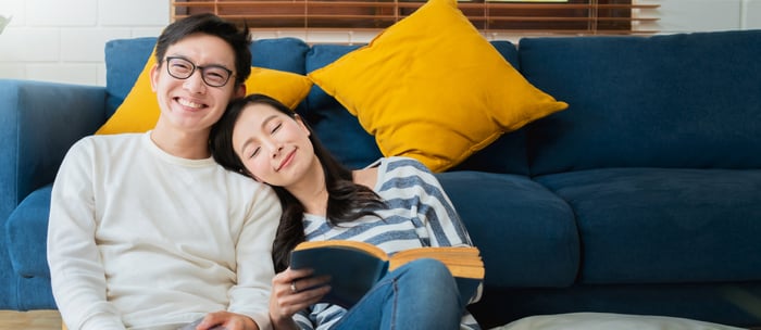 A couple is smiling, leaning against each other and a blue couch.